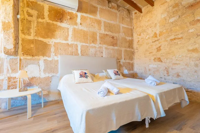 A bedroom with two beds, white bedding, and exposed stone walls.