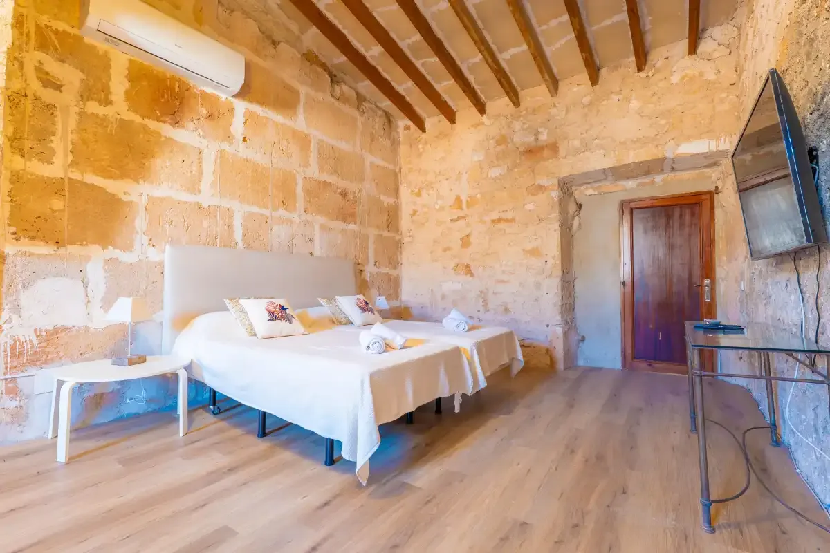 A bedroom with two beds, exposed ceiling beams, and a wooden door.