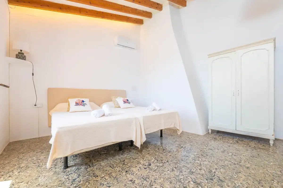 A bedroom with two beds, exposed wooden ceiling beams, and a white wardrobe.
