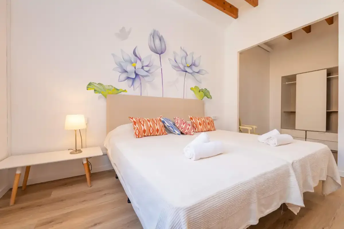 A bedroom with a double bed, colorful pillows, and floral wall art.