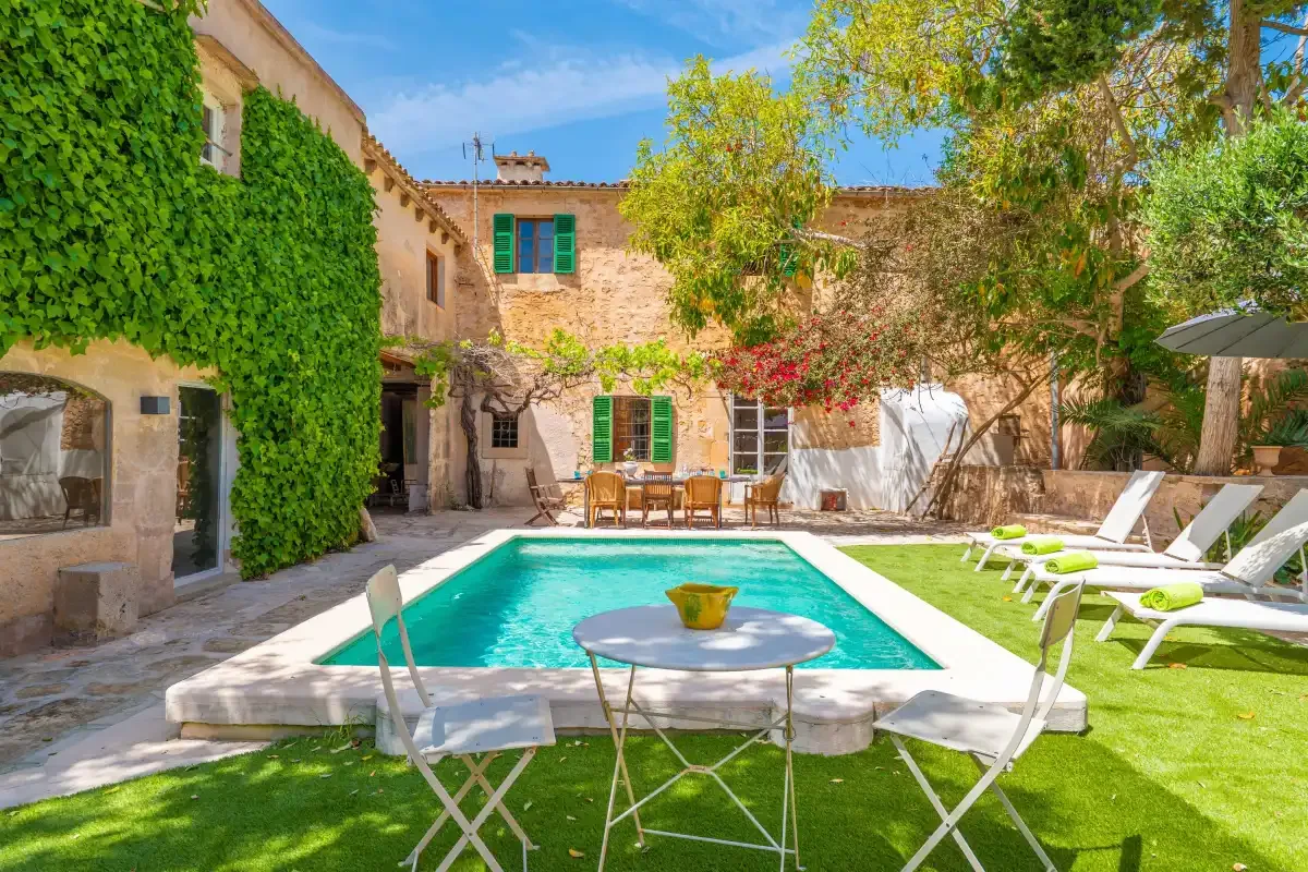 A courtyard pool sits beside a stone house, with outdoor seating and greenery.