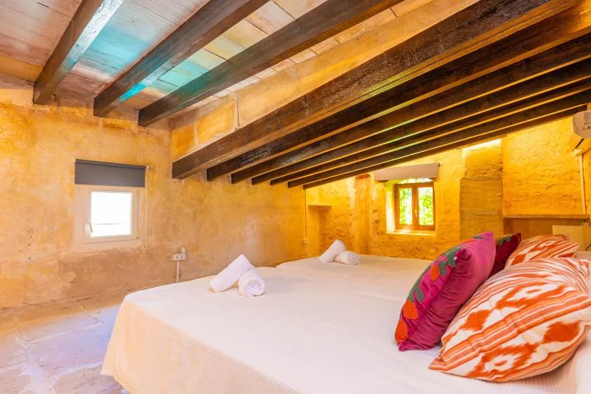 A bedroom with a bed beneath exposed wooden ceiling beams.
