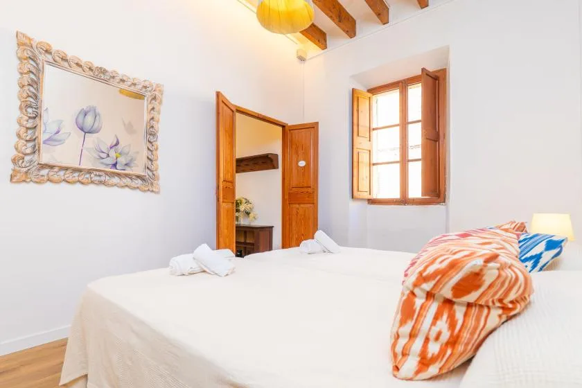 A bright bedroom with a white bed, wooden shutters, and framed floral artwork.