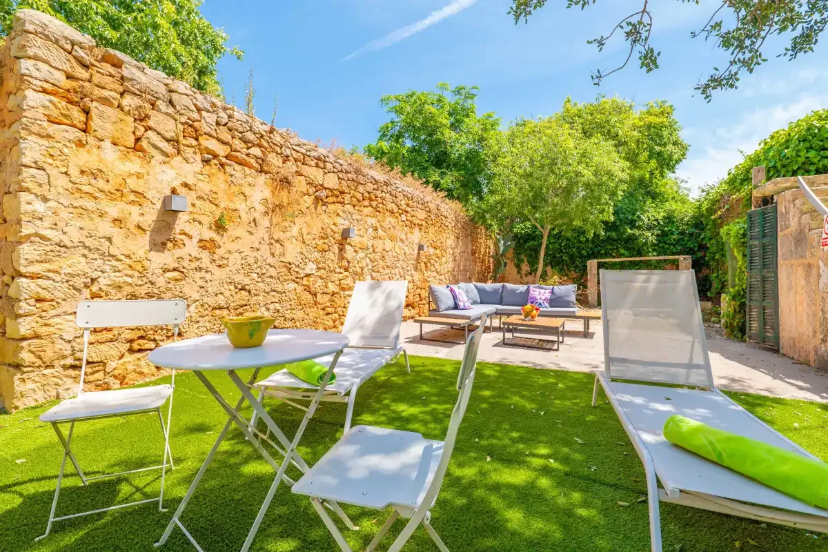 A sunny garden patio with outdoor seating and a table beside a stone wall.