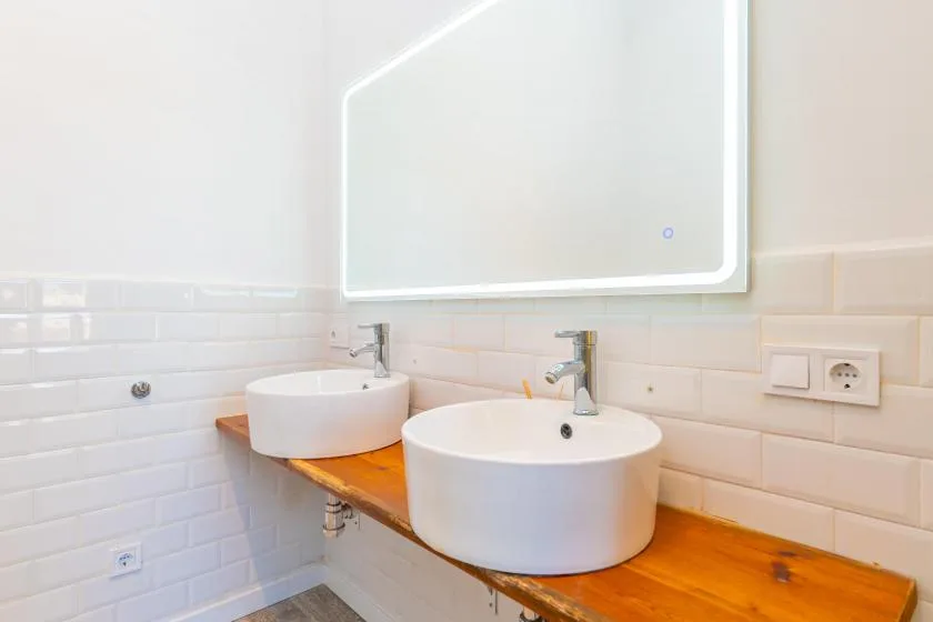 A bathroom vanity with two white vessel sinks beneath a large mirror.