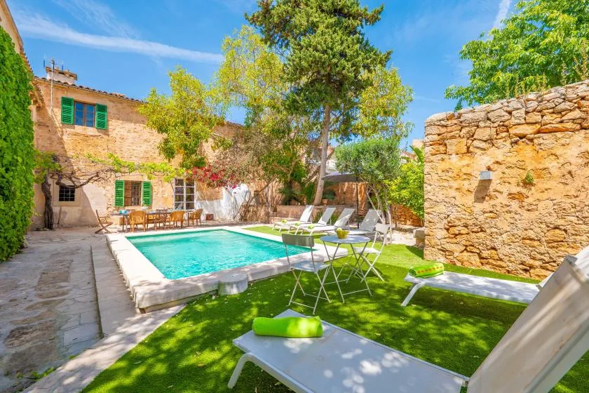 A garden patio with a swimming pool, outdoor seating, and stone walls.
