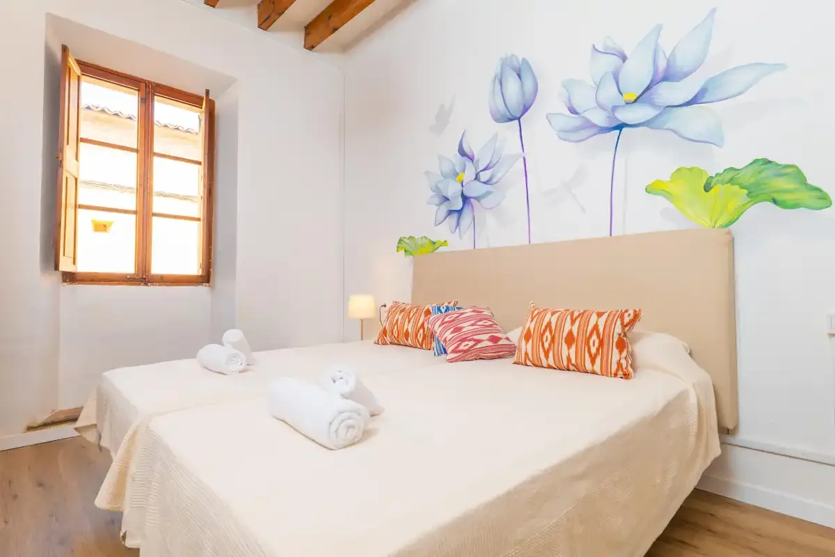 A bedroom with a double bed, patterned cushions, and a floral wall mural.