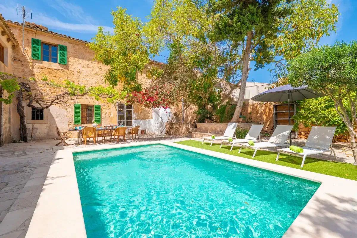 A courtyard pool sits beside a stone house and outdoor seating.