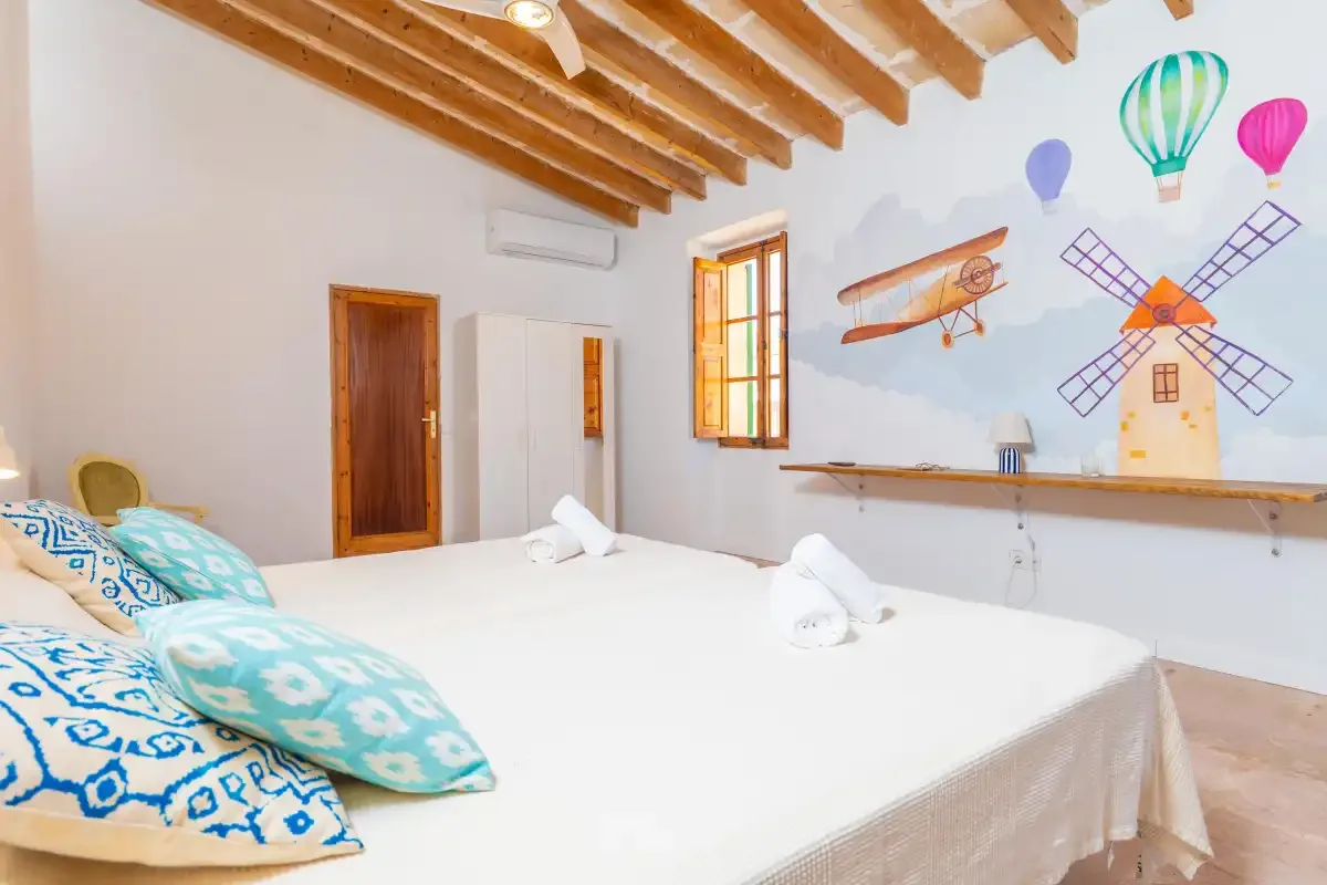 A bedroom with a bed, colorful patterned pillows, and a painted wall mural.