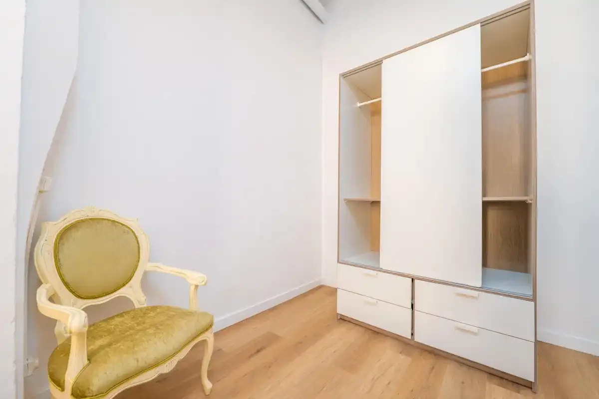 A bright room with a built-in wardrobe and an upholstered chair.