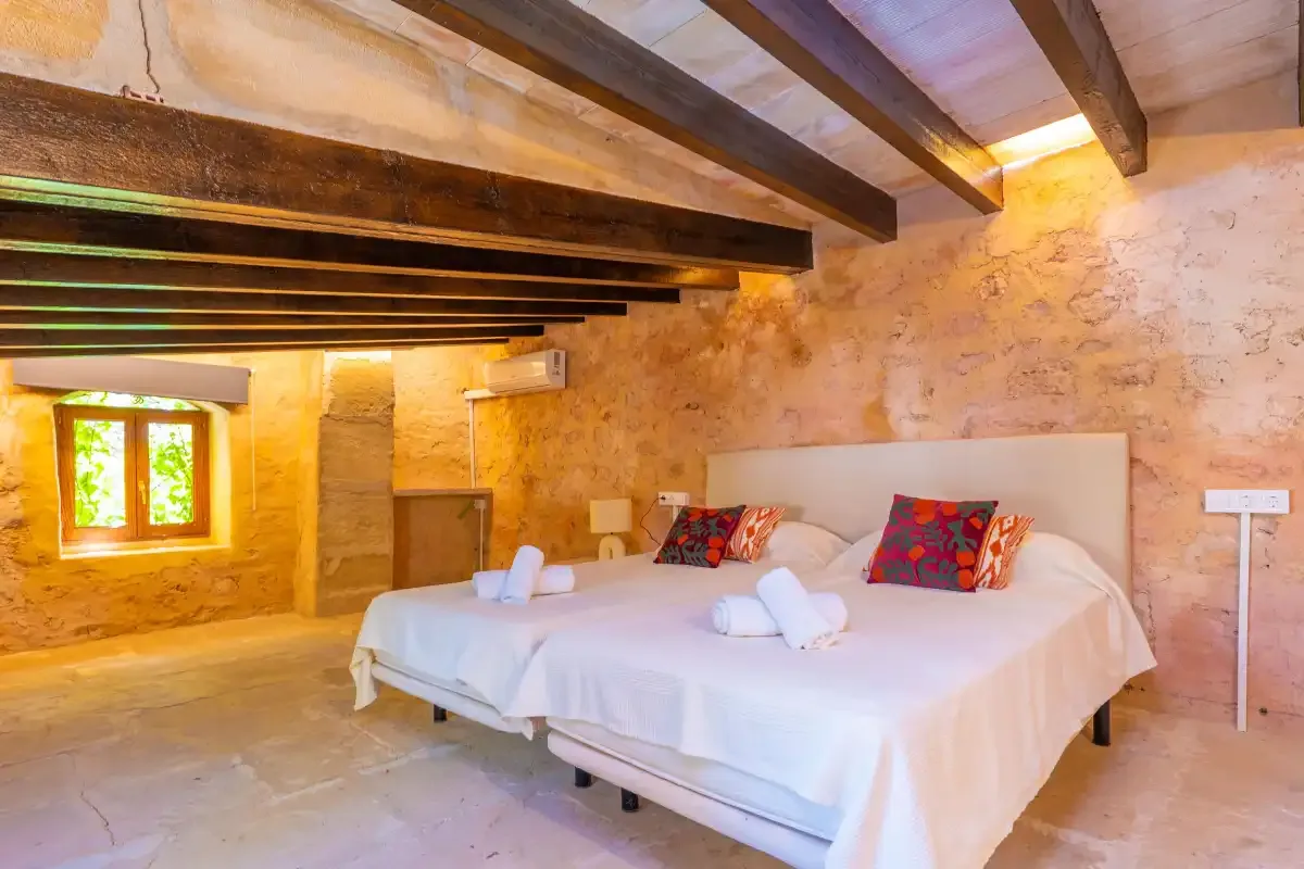 A bedroom with a large bed, colorful pillows, and exposed ceiling beams.