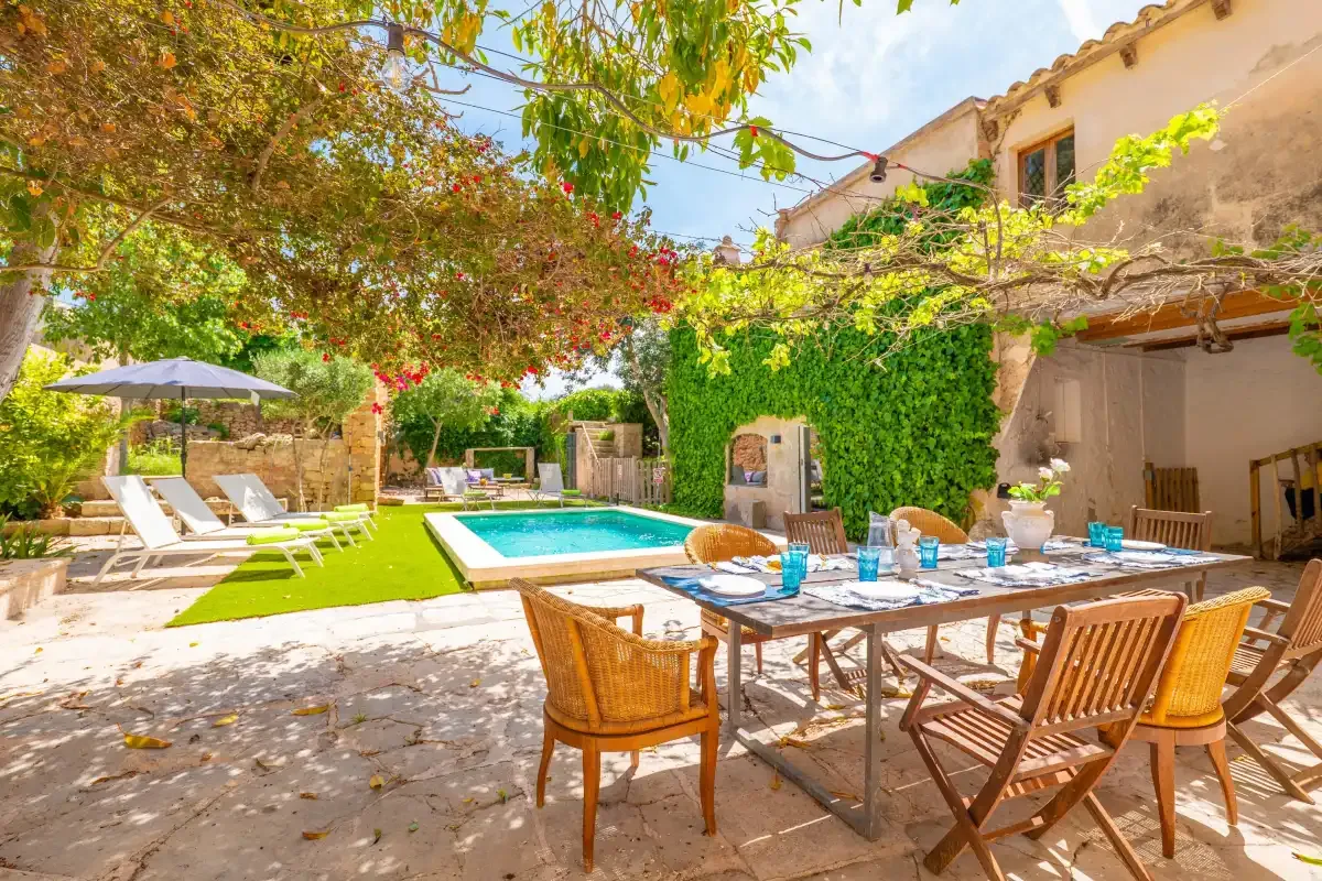 A sunny outdoor dining area beside a swimming pool and leafy garden.