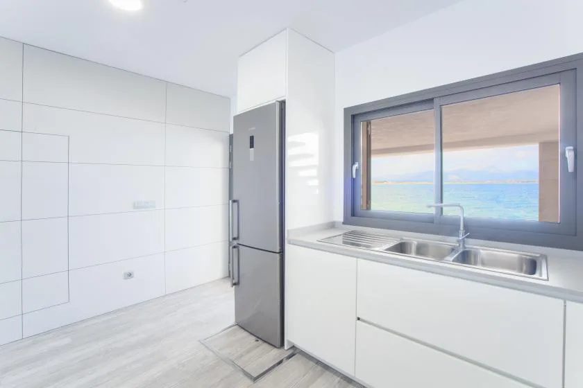 A bright kitchen with a refrigerator, sink, and ocean view through the window.