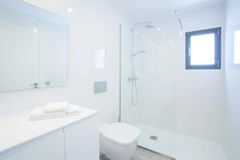 A bright bathroom with a glass shower, toilet, and vanity.
