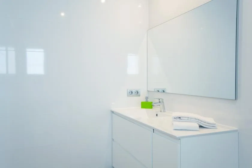 A bright bathroom vanity with a wide mirror and white countertop.