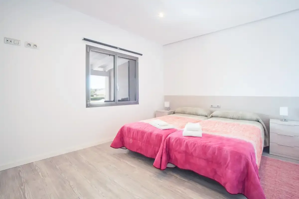 A bright bedroom with a bed covered in a pink bedspread.