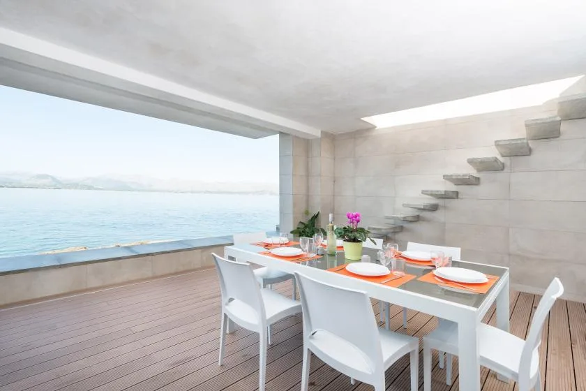 An open dining area with a table beside a broad view of the water.