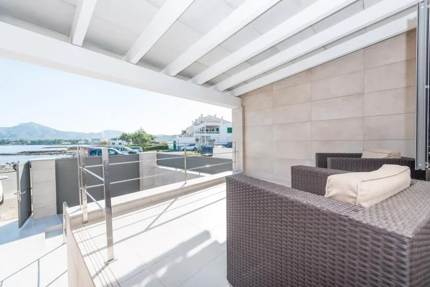 A covered terrace with woven seating overlooks nearby buildings and distant hills.