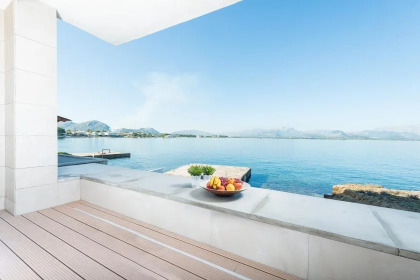 A waterfront terrace overlooks calm blue water, with fruit on the ledge.
