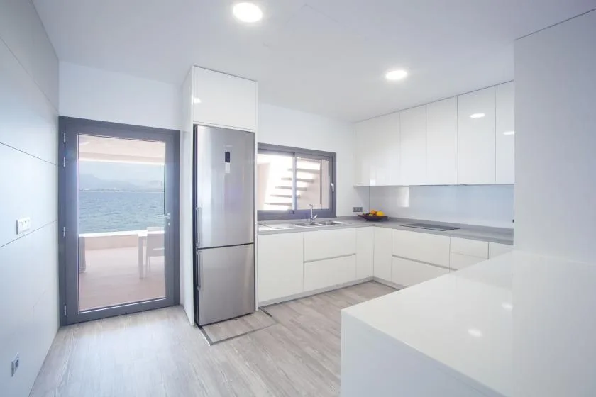 A bright modern kitchen with white cabinetry and a counter beside a glass door.
