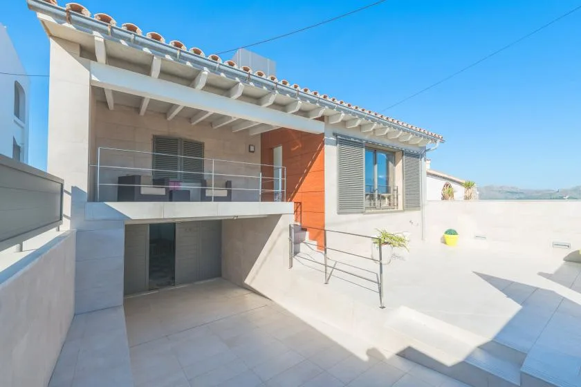 A modern house opens onto a sunlit terrace with a glass-railed balcony.