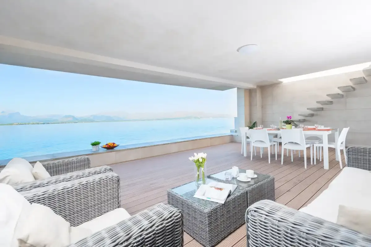 A covered terrace with seating and a dining table overlooks the sea.