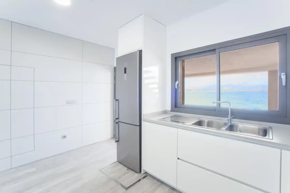 A bright kitchen with a sink beneath a window overlooking the sea.