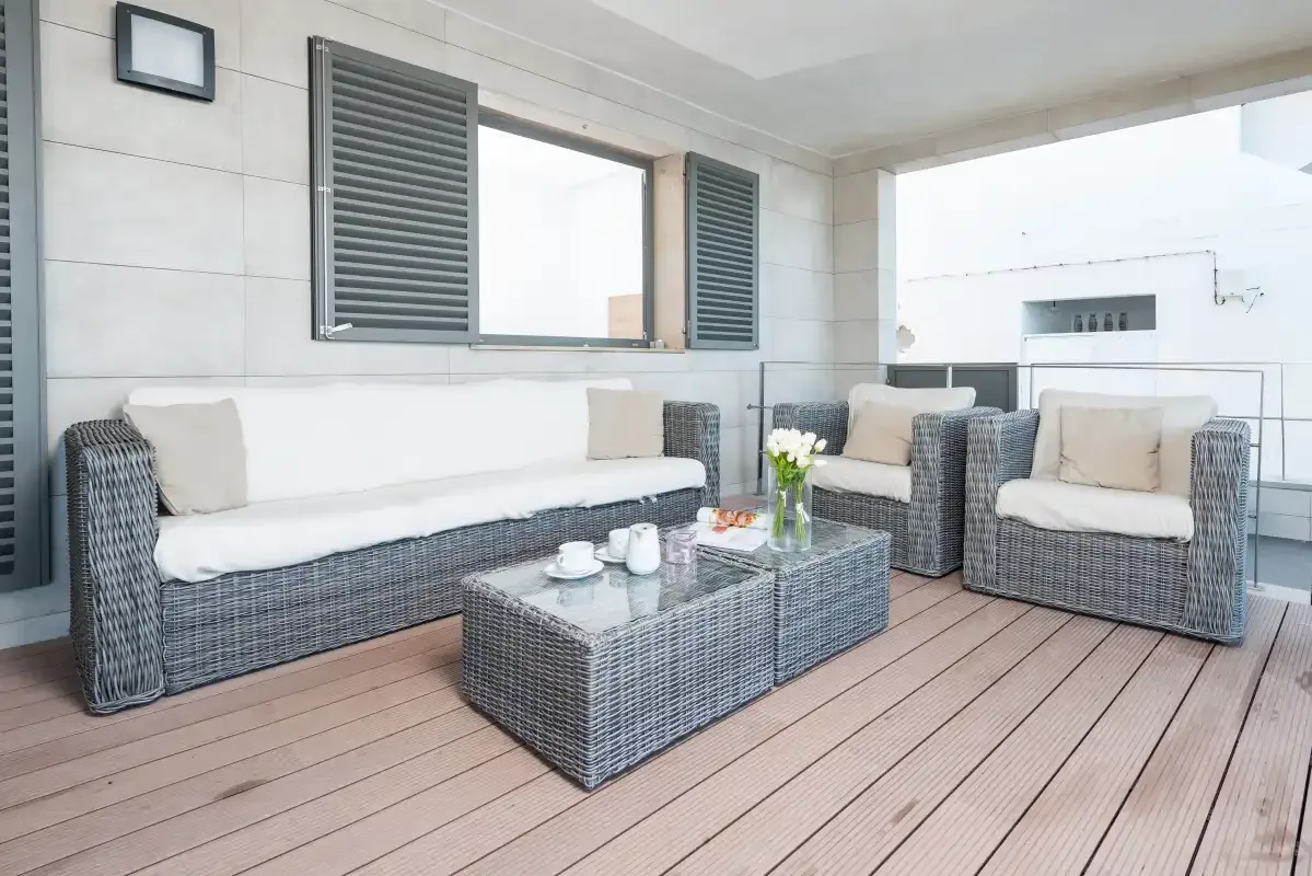 A covered patio seating area with woven furniture and a glass-topped table.