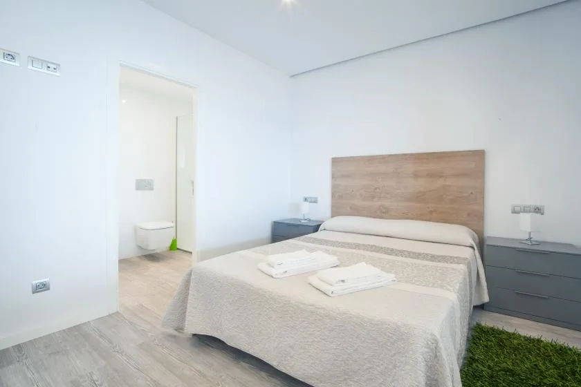 A bright bedroom has a double bed with folded towels and a wooden headboard.