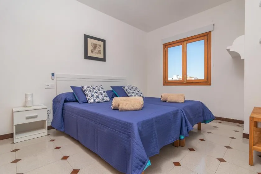 A bedroom with blue bedding, patterned pillows, and a wooden-framed window.