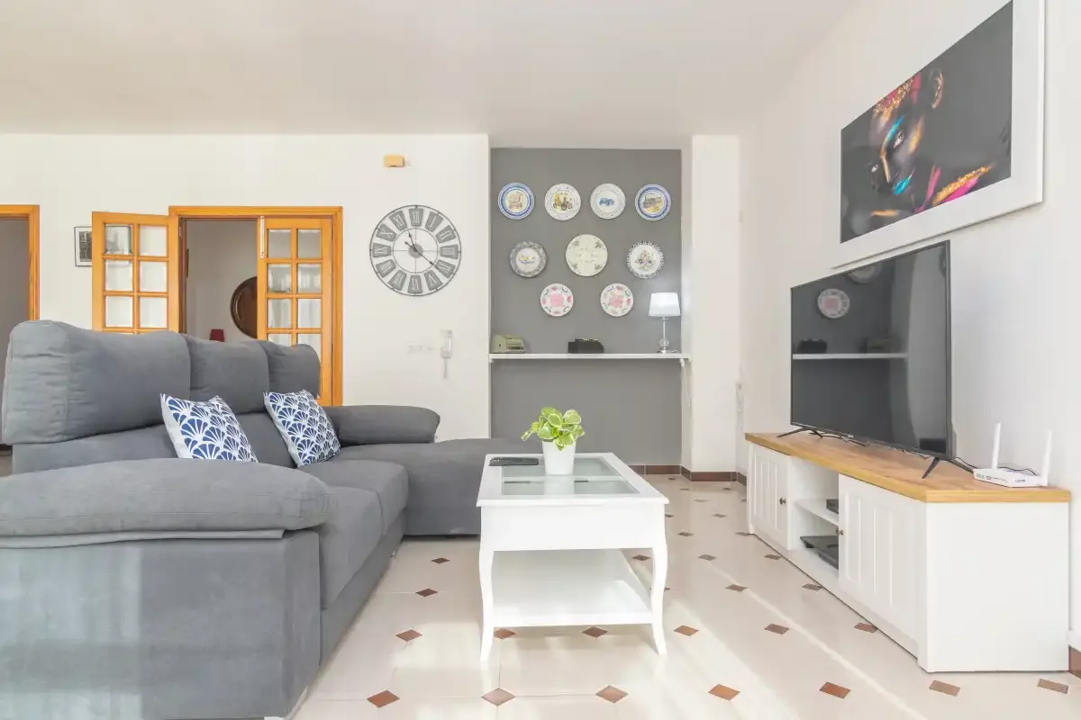 A living room with gray seating, a white coffee table, and a television.