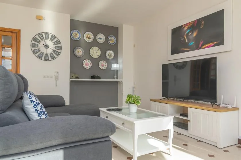 A bright living room with gray seating, a coffee table, and a television.