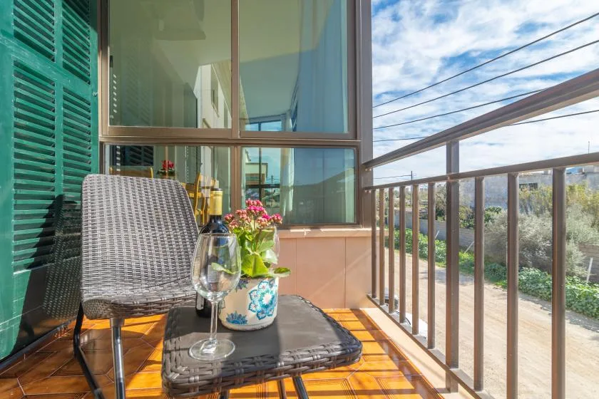 A small balcony with seating and a glass railing overlooks a green landscape.