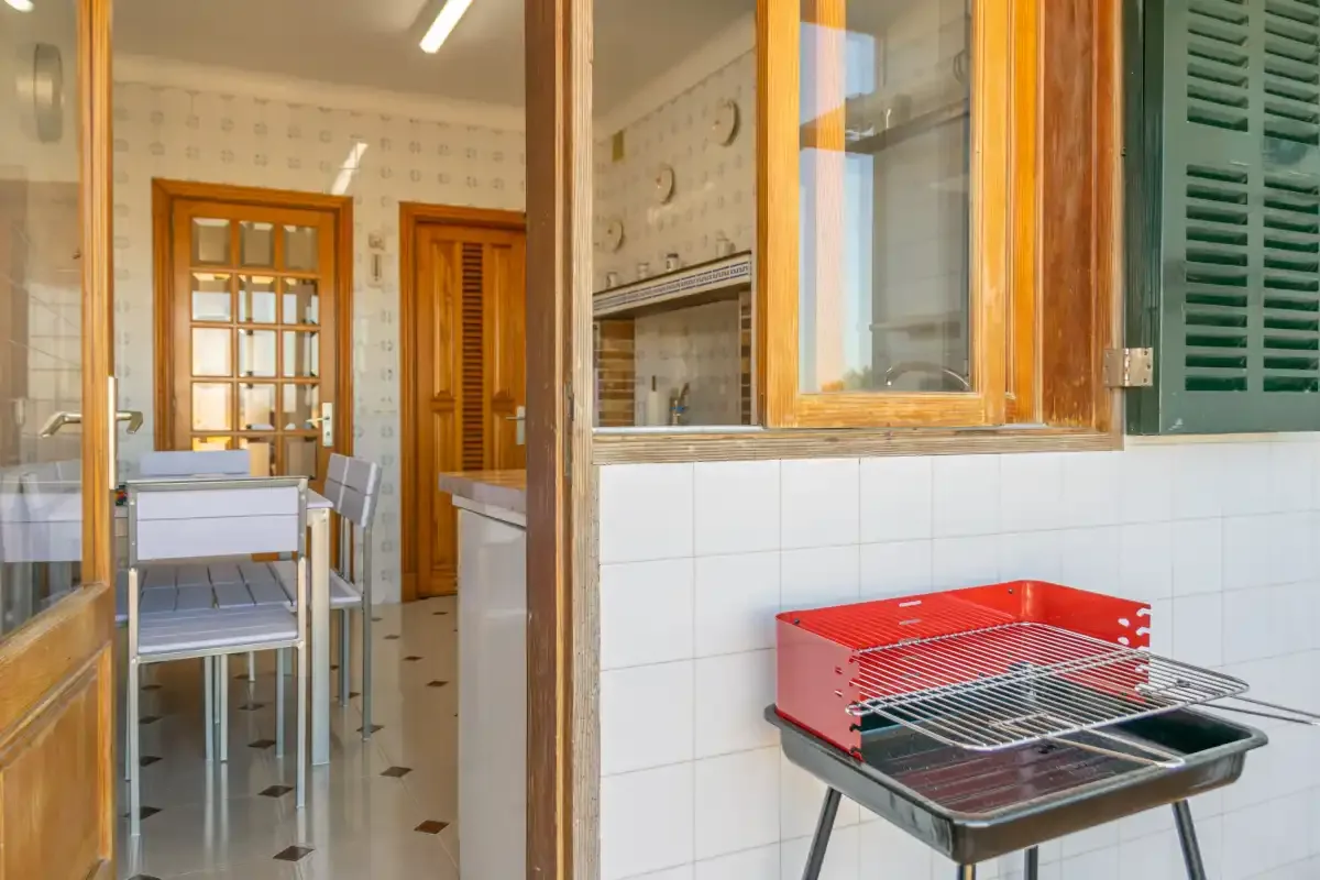 A tiled kitchen area with a red portable grill beside a dining table.