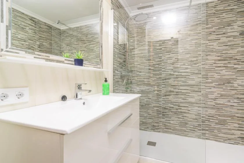 A bathroom with a sink vanity, large mirror, and tiled shower area.