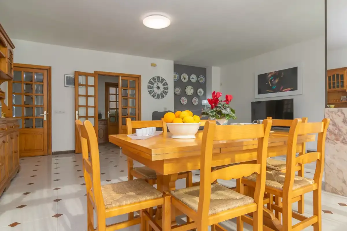 A dining area with a wooden table and chairs, fruit bowl, and wall decorations.