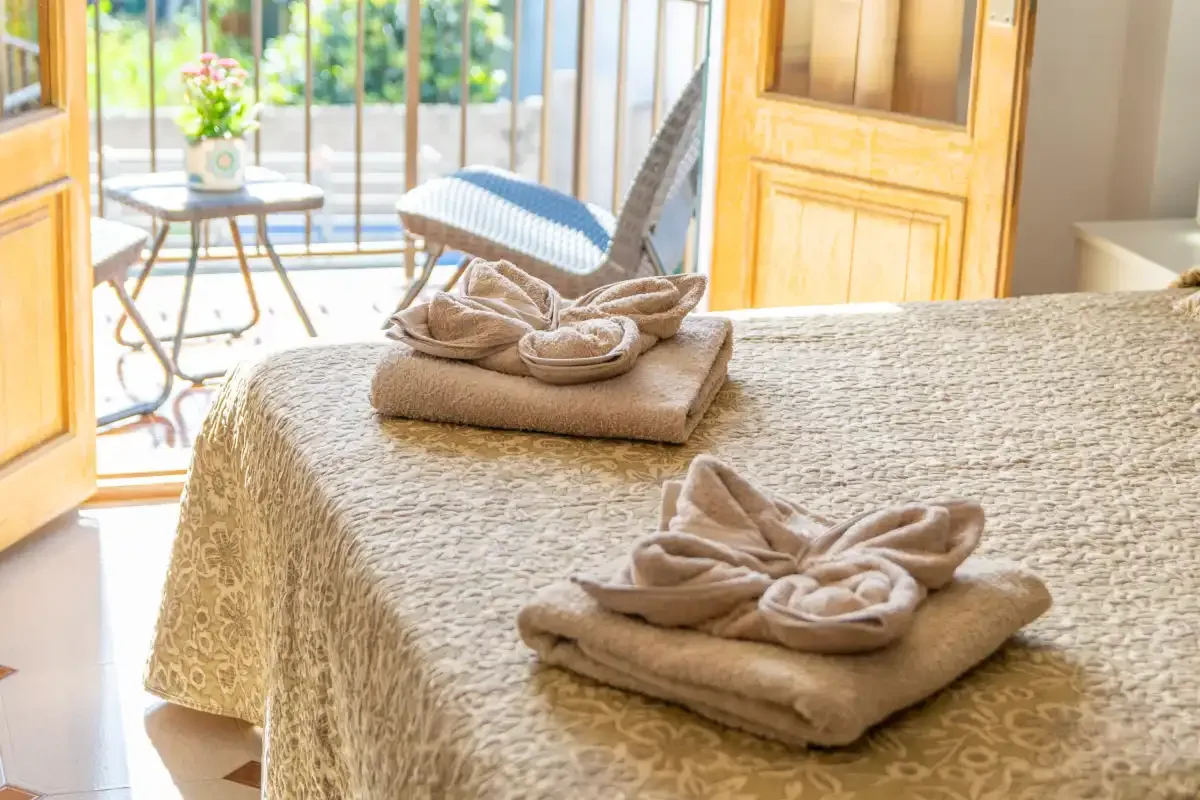 A bedroom with a bed covered in a patterned bedspread and folded towels.