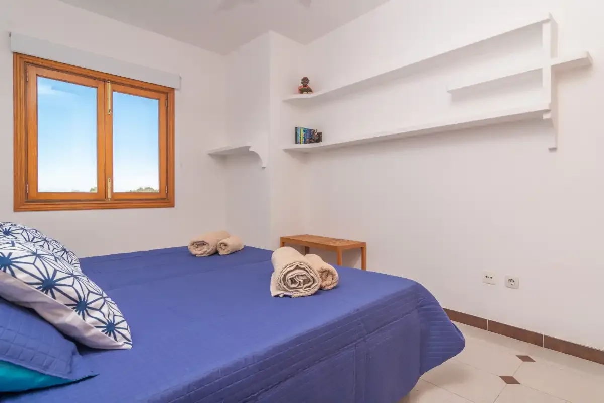 A bedroom with a blue-covered bed beside a wooden-framed window.