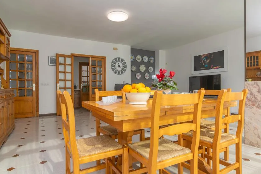 A dining room with a wooden table and chairs, with fruit and flowers on the table.