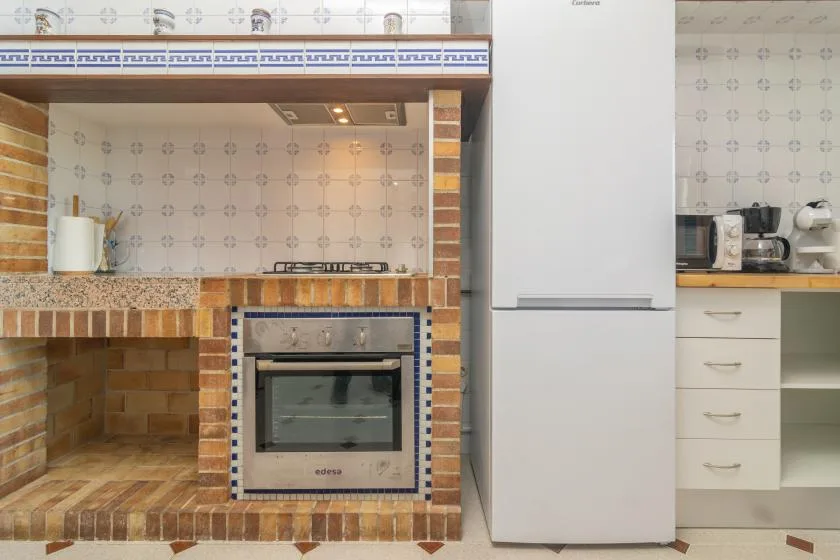 A tiled kitchen with a brick-faced cooking area and a tall refrigerator.