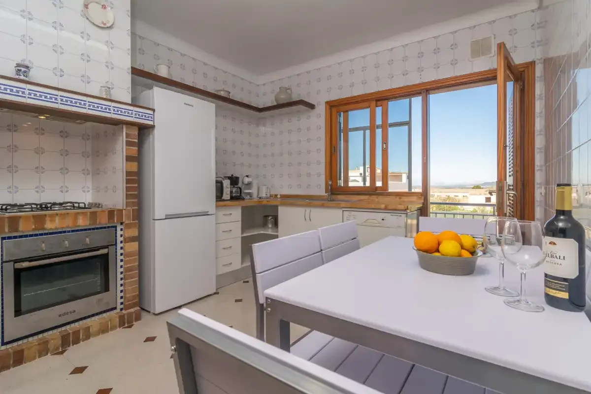 A tiled kitchen with a dining table and open windows overlooking the landscape.