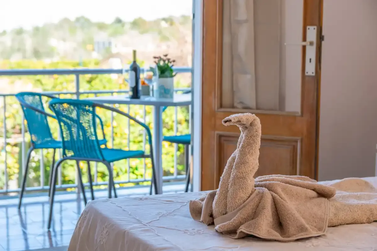 A bedroom opens onto a balcony with outdoor seating and a towel arranged on the bed.