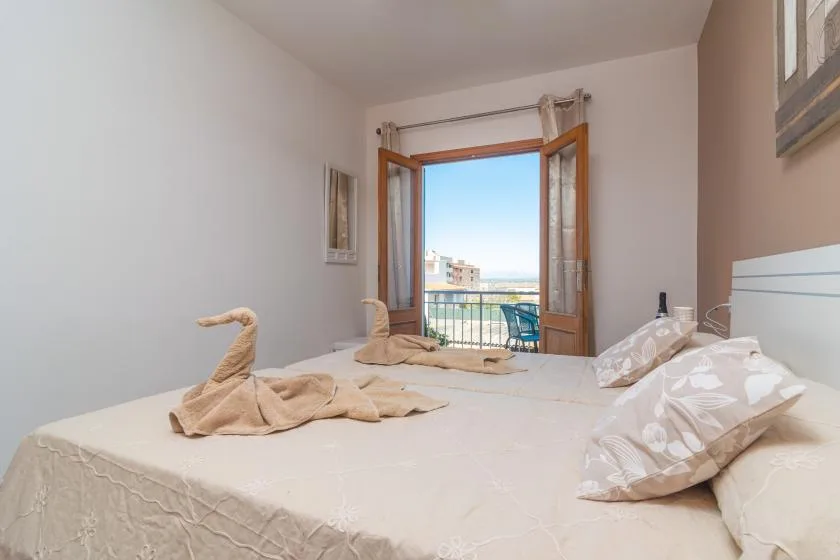 A bedroom with a bed and an open balcony door overlooking the city.