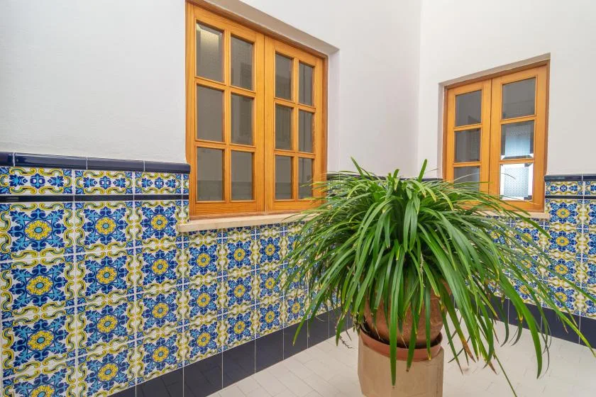 A tiled interior wall with wooden windows and a potted leafy plant.
