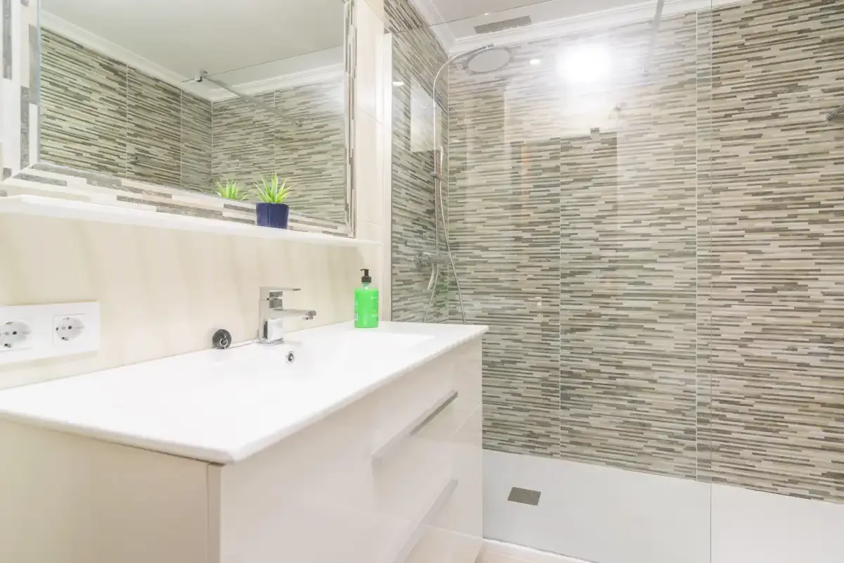 A bright bathroom with a white vanity and tiled shower.