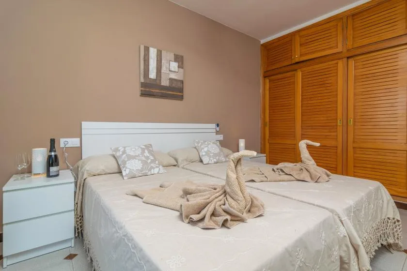 A bedroom with two beds, folded towels, and wooden louvered closet doors.