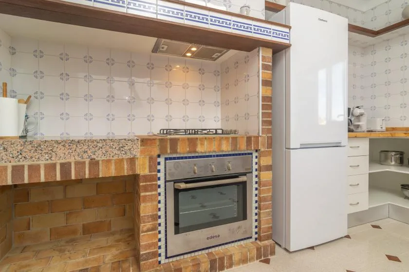 A tiled kitchen with a built-in oven, stovetop, and white refrigerator.
