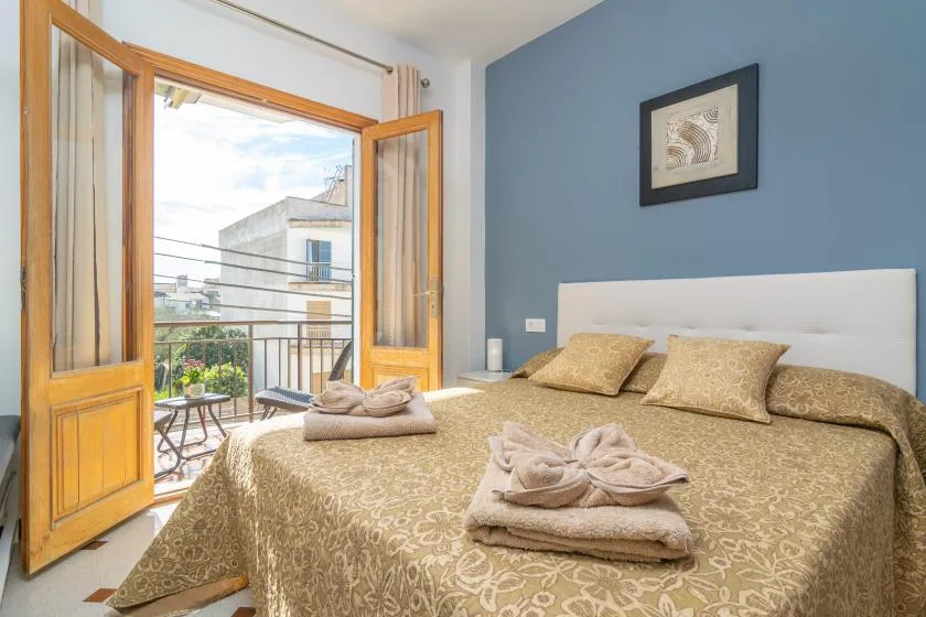 A bedroom with a neatly made bed and open wooden doors to a balcony.