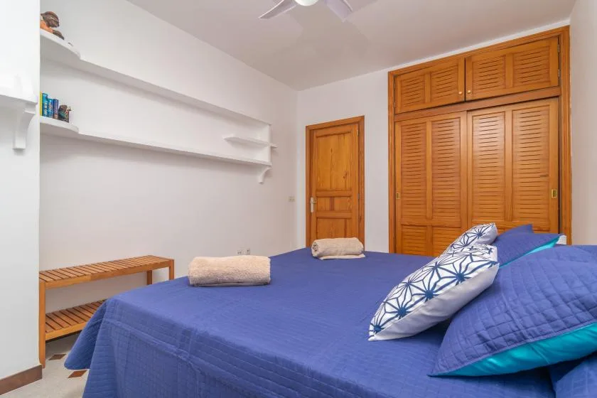 A bedroom with a blue bedspread, wooden doors, and wall shelves.