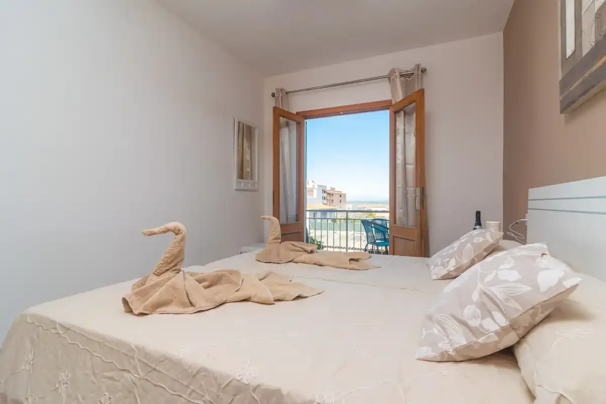 A bedroom with a bed facing open balcony doors and a view outside.